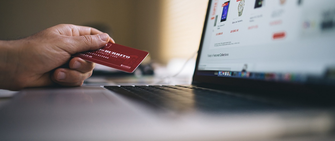 A person holding a credit card next to a laptop with an e-commerce site on the screen